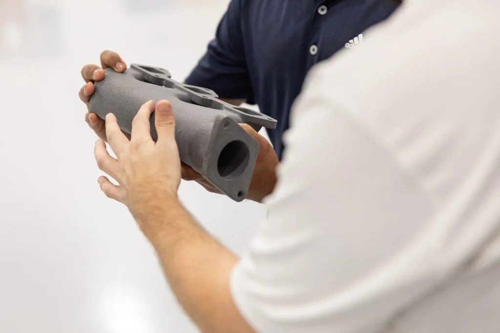 Endeavor 3D employees holding a Nylon PA12 3D printed automotive part
